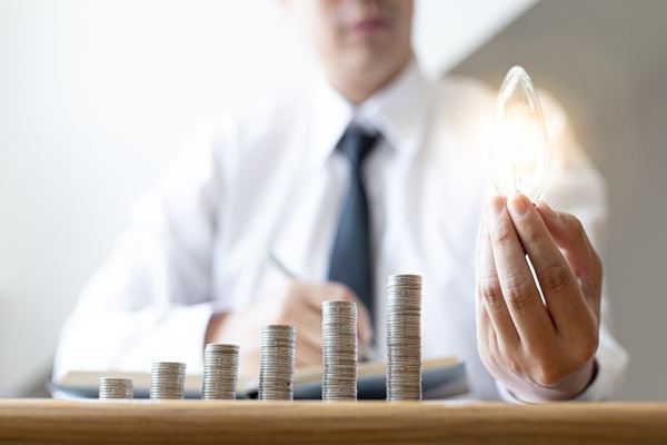 Young,Businessman,Holding,A,Light,Bulb,And,Coins,Or,Money